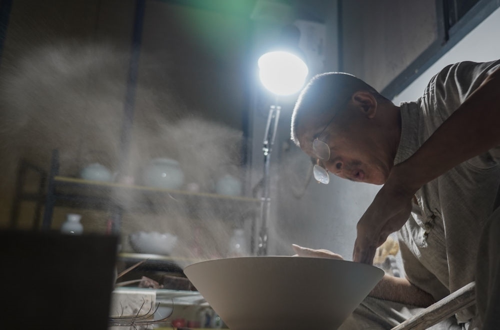 ↑ 在景德鎮(zhèn)，手工匠人吹去坯內(nèi)的泥土（2021年7月14日攝）。