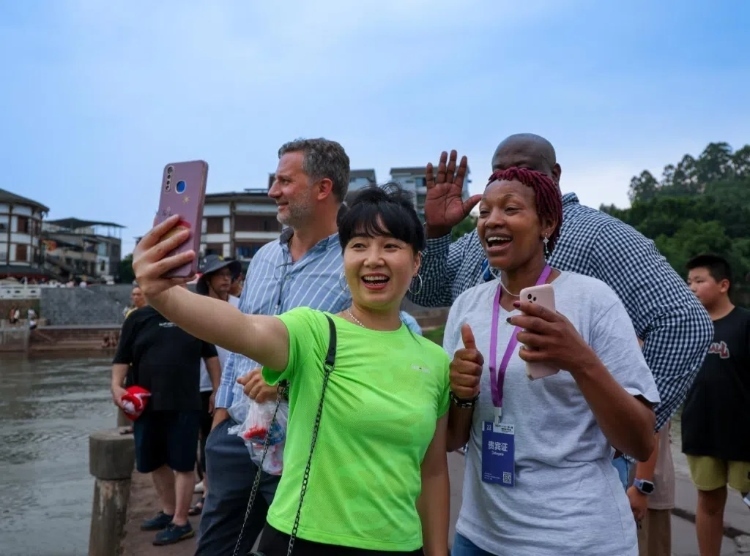 2024“一帶一路”媒體合作論壇聯(lián)合采訪調(diào)研行成員在樂山蘇稽古鎮(zhèn)與游客合影留念。本報記者 伊霄攝